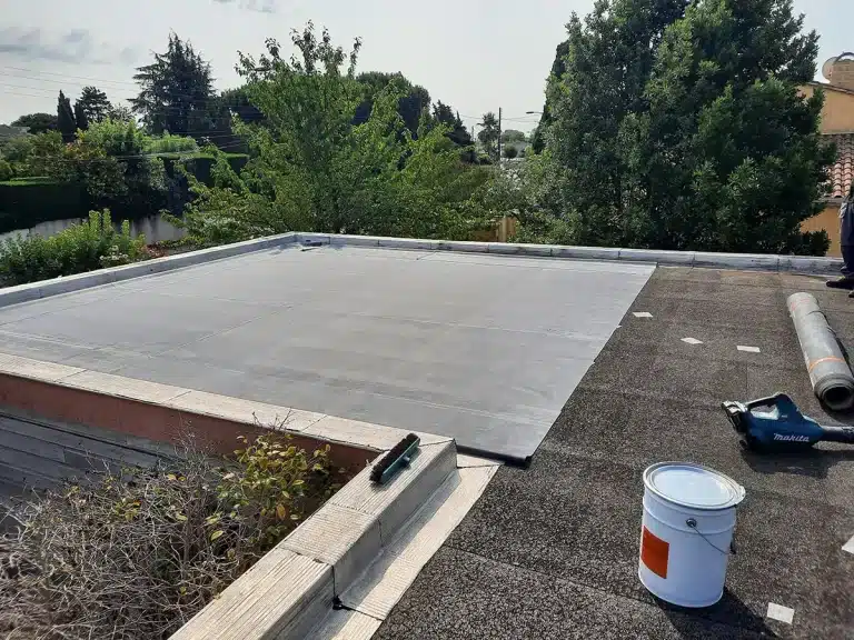Photo d'un toit plat vue de dessus. Une membrane d'étanchéité est posée pliée sur le toit. On voit un pot de colle sur le côté